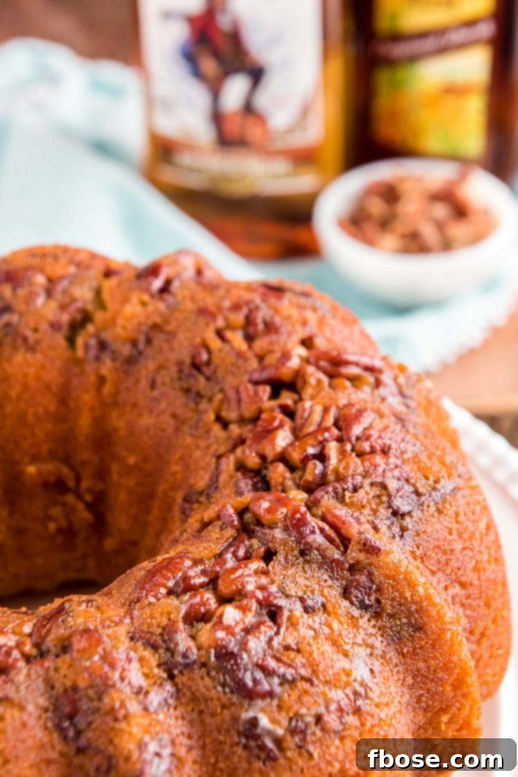 Close up photo of a rum cake on a white cake stand with bottles of rum in the background.