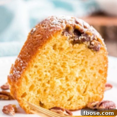 Close up photo of a slice of rum cake on a white plate with a blue napkin in the background.