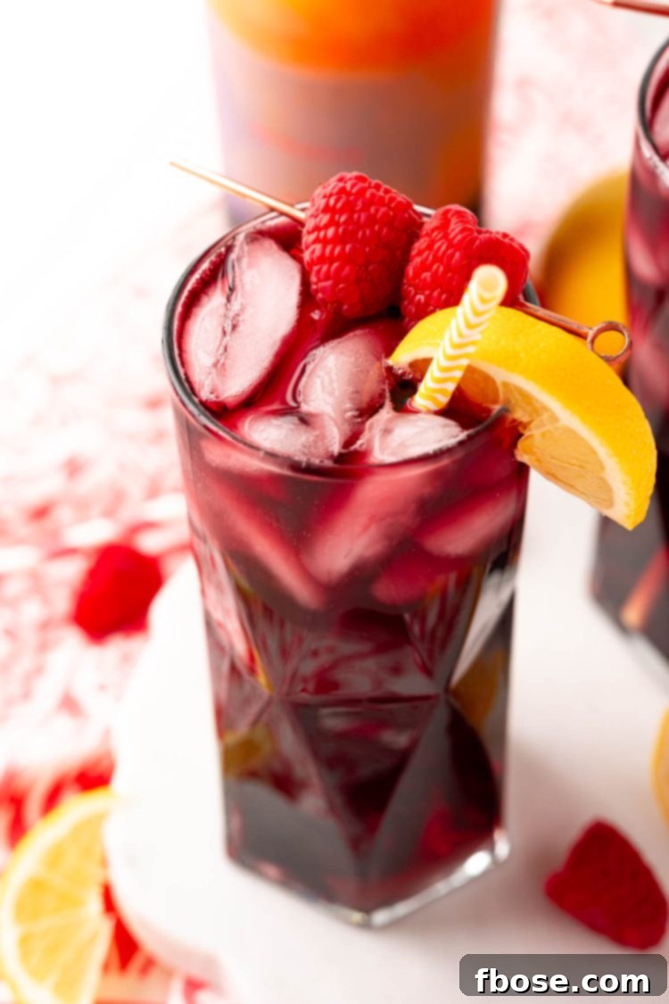 Close up photo of a red wine spritzer garnished with raspberry and lemon wedge.