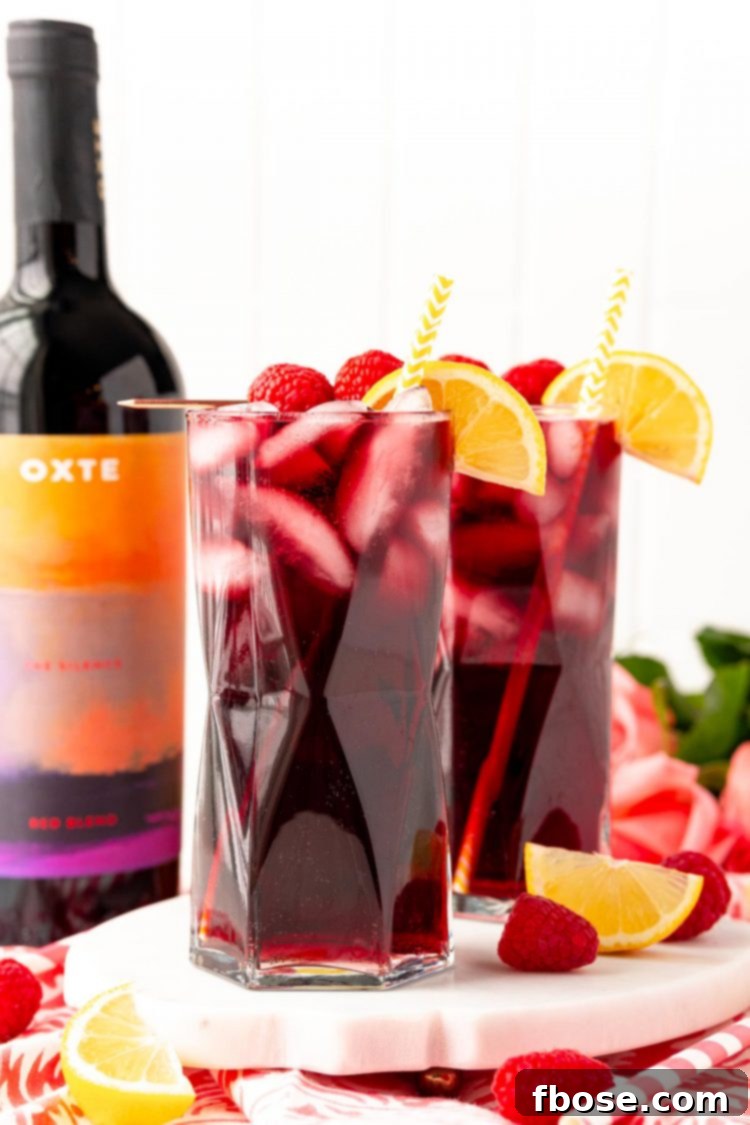 Straight on photo of two glasses filled with red wine spritzers on a marble tray with a bottle of red wine in the background.