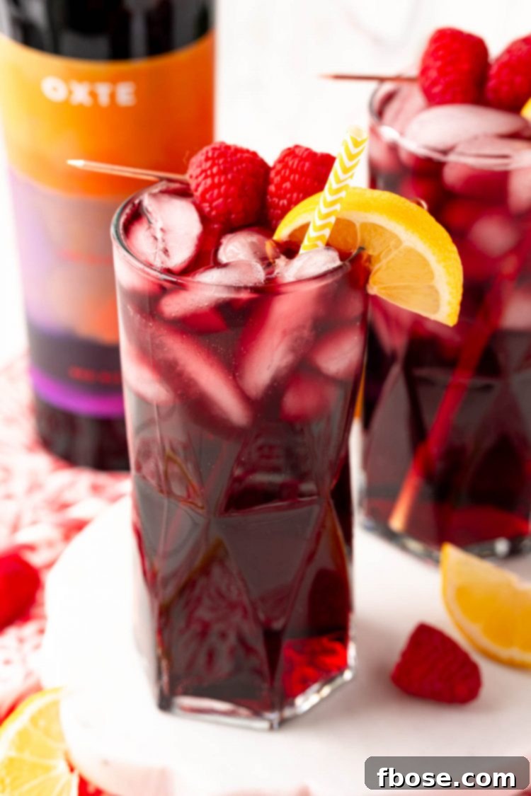 Close up photo of a red wine spritzer garnished with raspberries and lemon wedge.