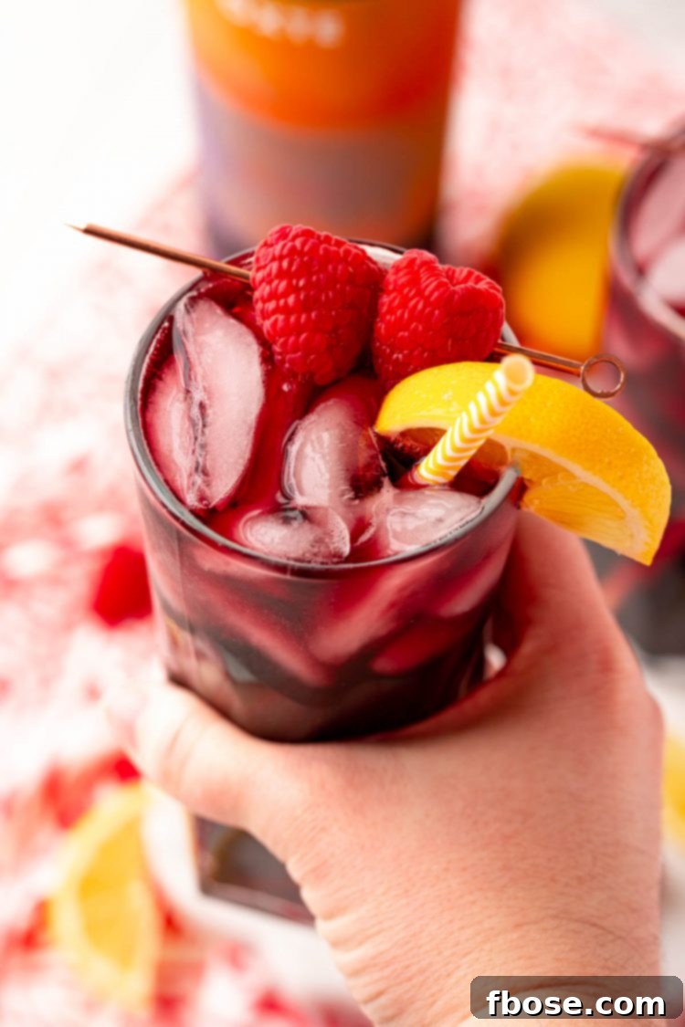A woman's hand holding a red wine spritzer to the camera.