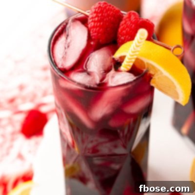 Close up photo of a red wine spritzer garnished with raspberry and lemon wedge.