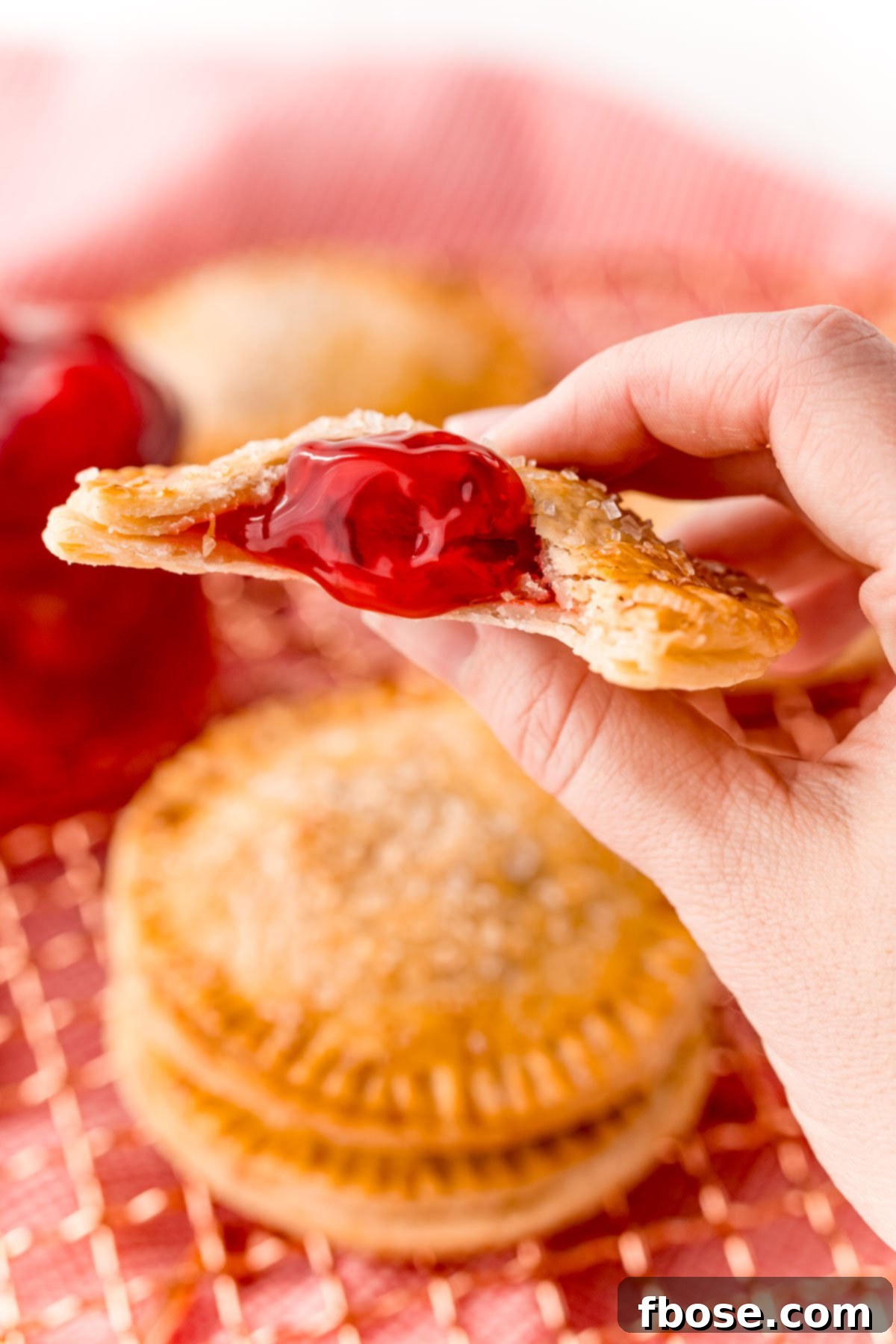 A woman's hand holding a cherry hand pie to the camera. Perfect single-serving dessert.