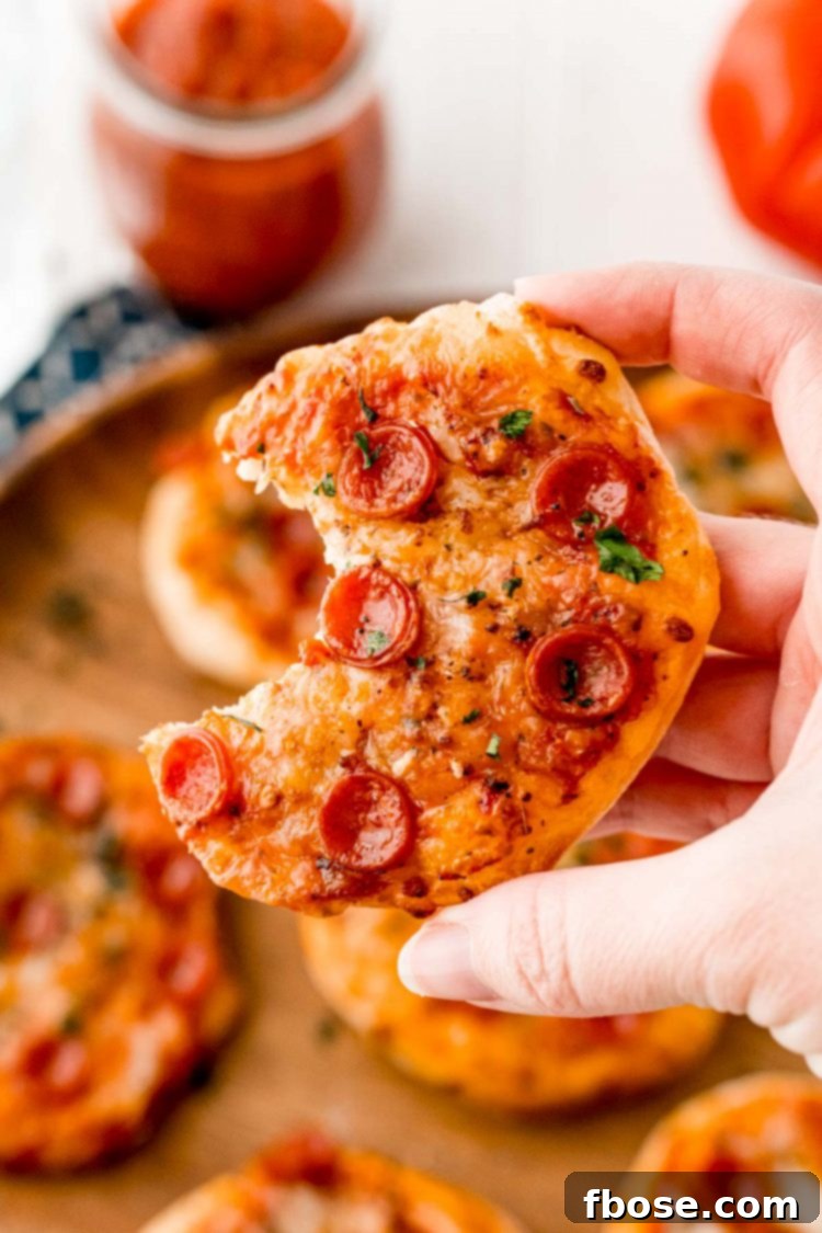 A woman's hand holding a mini pizza with a bite taken out of it.