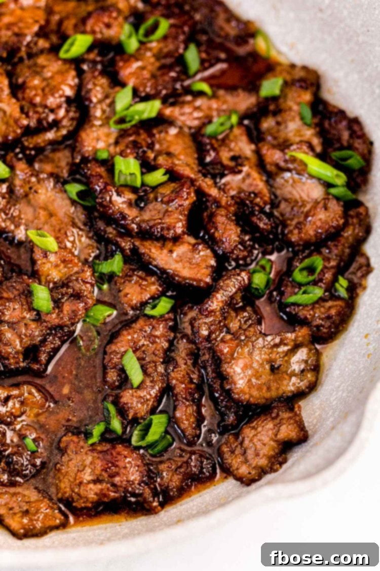 Close up photo of Mongolian beef in a pan garnished with scallions. 