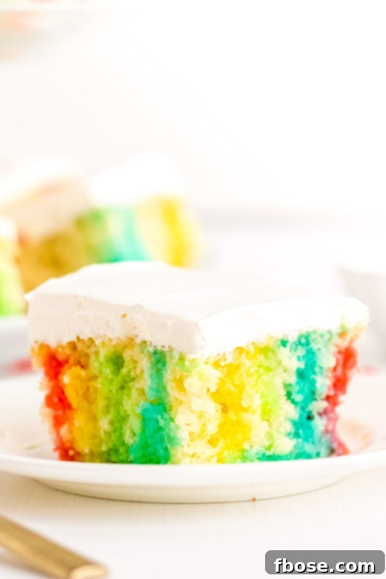 This Rainbow Jello Poke Cake is easily made using a boxed white cake mix and jello to create a fun, light dessert filled with vibrant colors and topped with fluffy whipped cream.