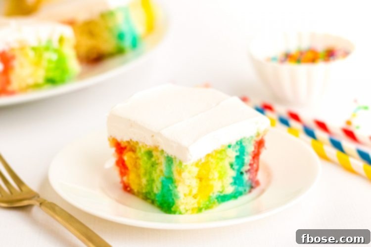 Close up photo of a slice of rainbow jello poke cake on a white plate, showing the vibrant colored jello layers within the moist cake.