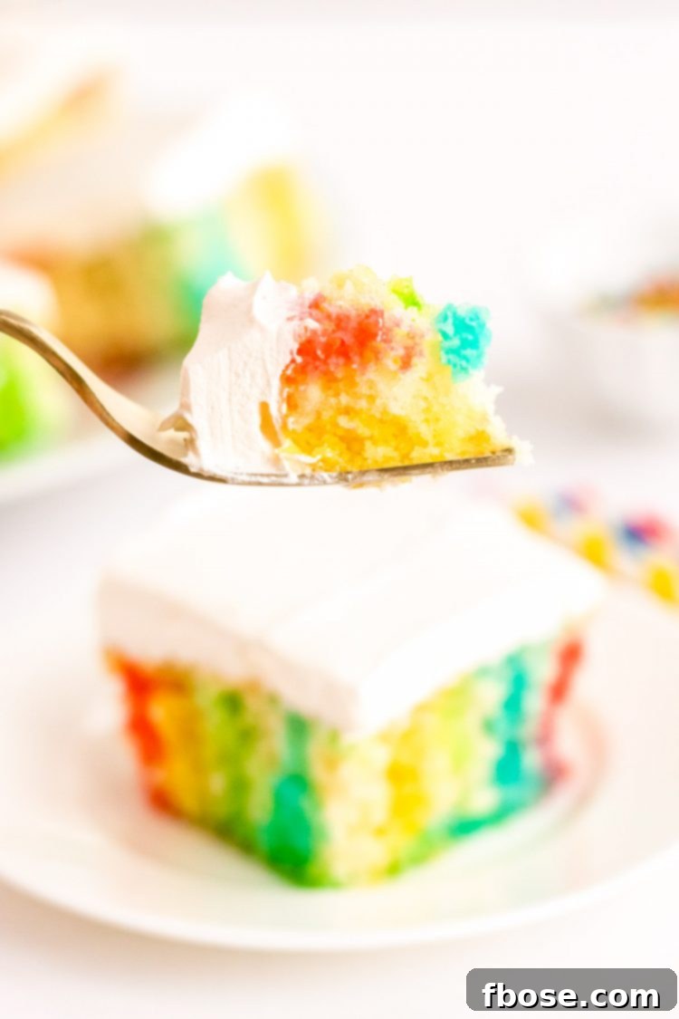 A fork holding a bite of rainbow jello poke cake up to the camera, showing the colorful layers.