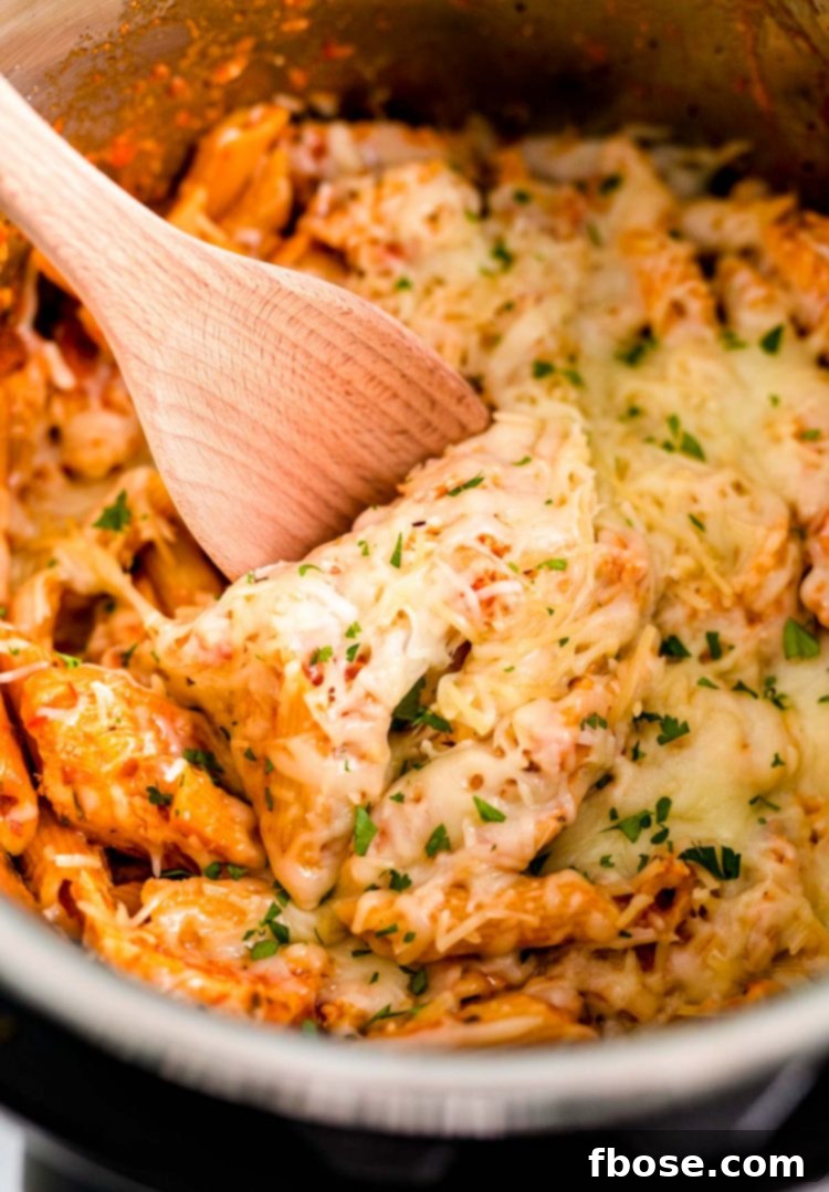 Close up photo of a wooden spoon scooping into an instant pot with rich and cheesy chicken parmesan pasta.