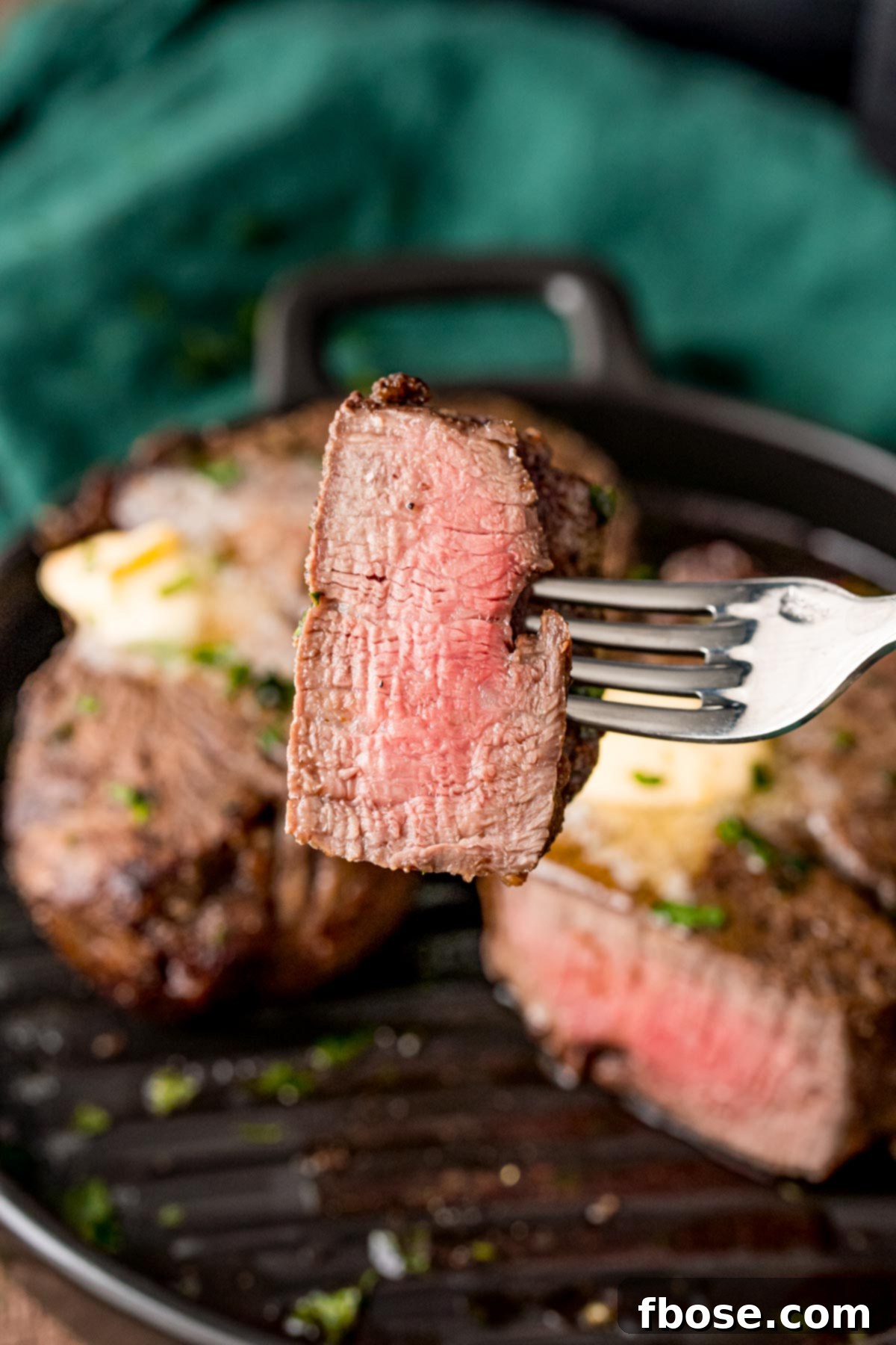 A fork with a piece of steak on it being held towards the camera.