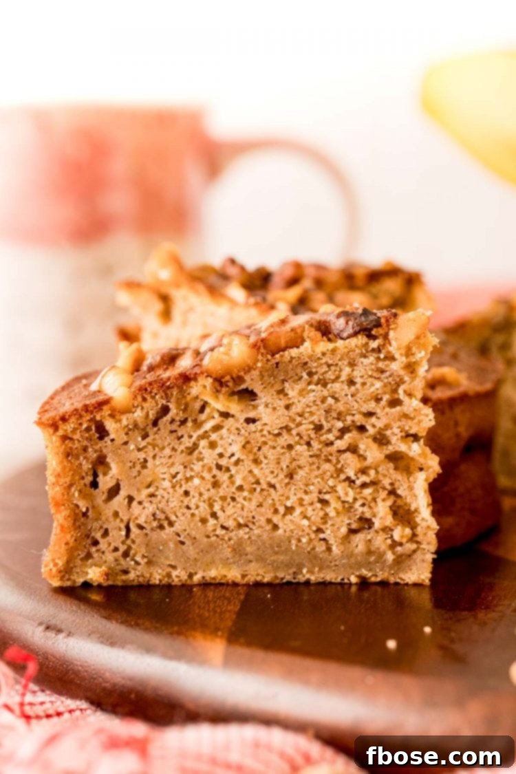 A close-up shot of a single slice of moist air fryer banana bread, revealing its tender texture and golden crust, elegantly placed on a wooden cutting board.