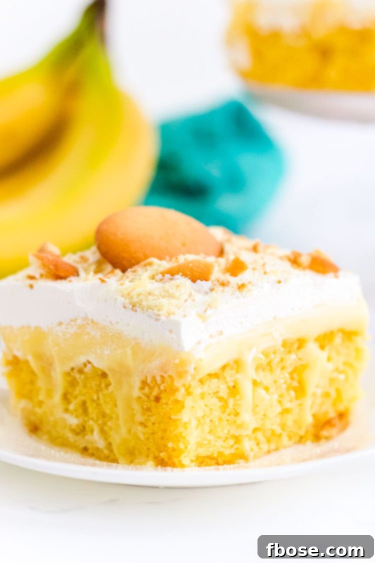 Close up of a slice of banana poke cake on a white plate with bananas in the background.