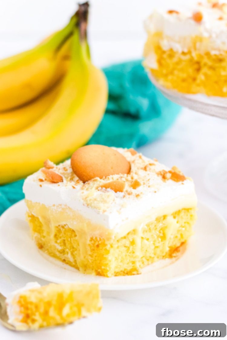 A slice of banana cream poke cake on a white plate with a teal napkin behind it.