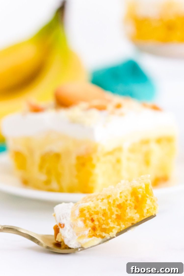 A fork with a bite of banana pudding poke cake on a white surface.