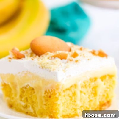 Close up of a slice of banana poke cake on a white plate with bananas in the background.