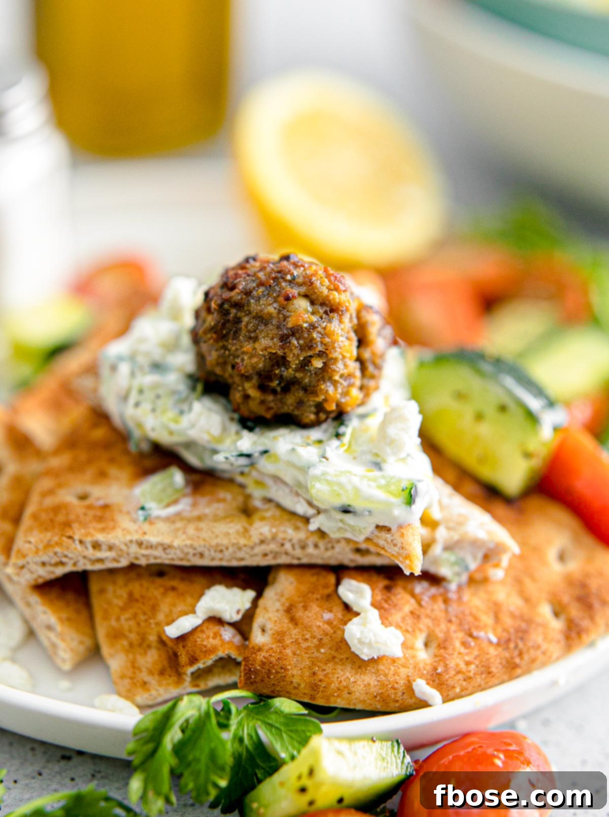 Greek meatballs with a dollop of tzatziki sauce on pita bread, garnished with fresh dill.