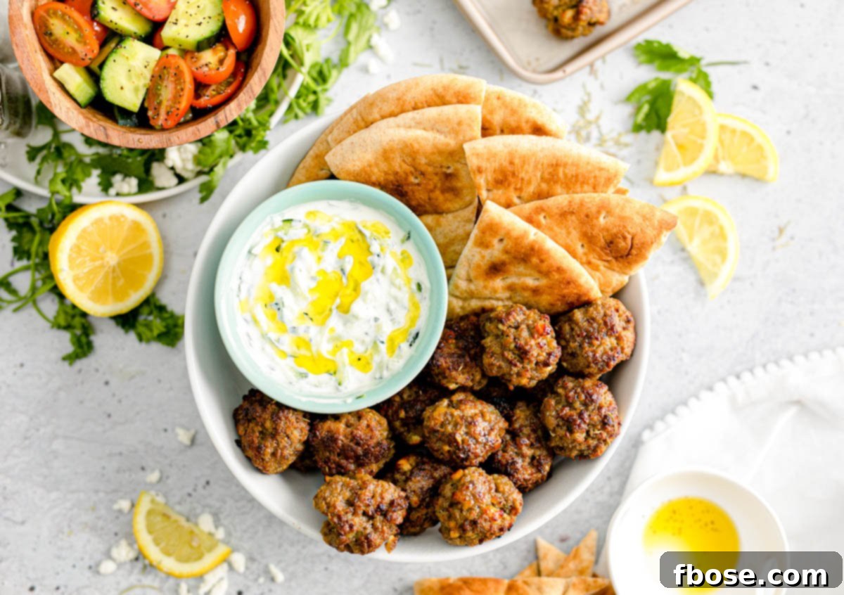 Overhead photo of Greek meatballs artfully arranged with tzatziki sauce in a bowl and fresh pita bread, ready for serving.