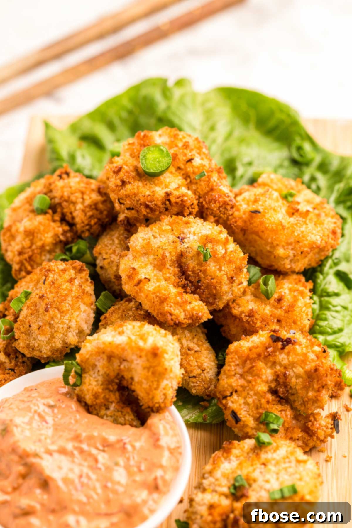 Close up photo of crispy air fryer shrimp on a bed of lettuce with dipping sauce.