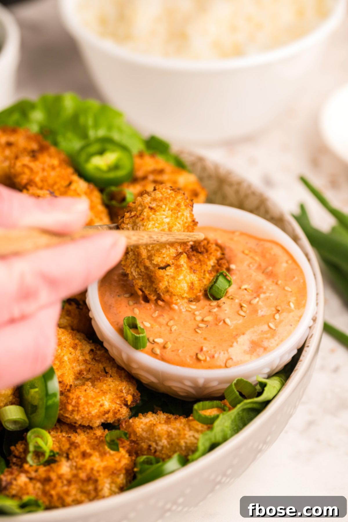 A piece of crispy shrimp being dipping in a sauce.