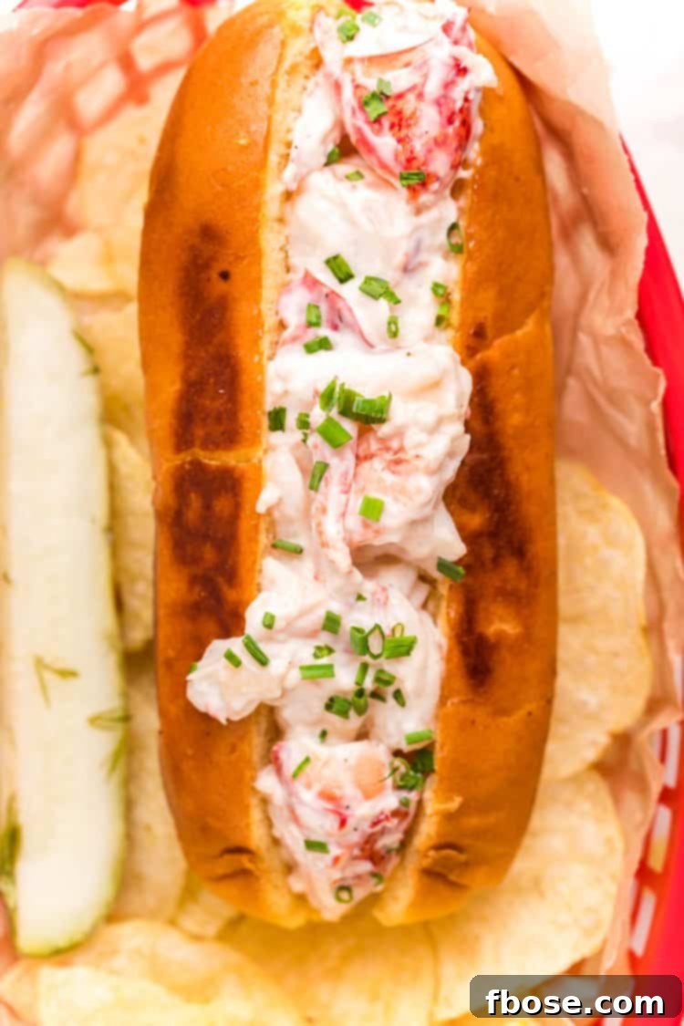 Close up photo of a lobster roll in a red basket with chips and a pickle.