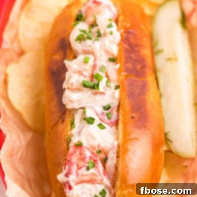 Close up photo of a lobster roll in a red basket with chips and a pickle.