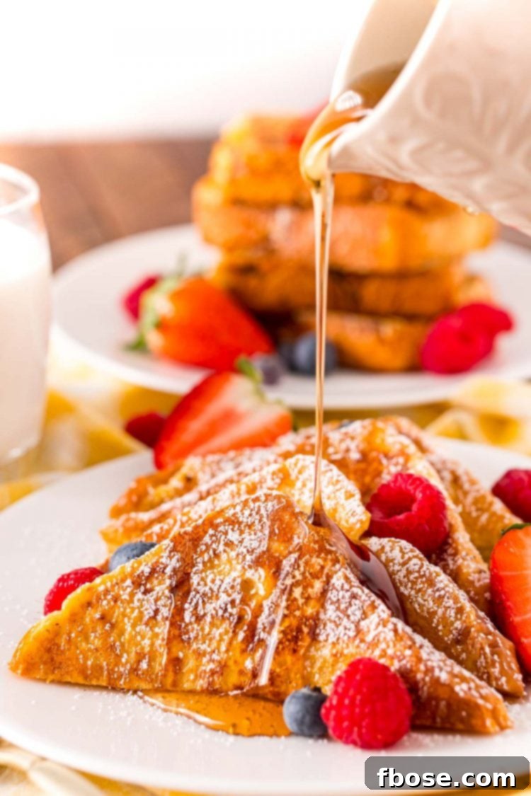 Maple syrup being poured over the top of a plate of French toast with fresh berries, creating a tempting breakfast scene.