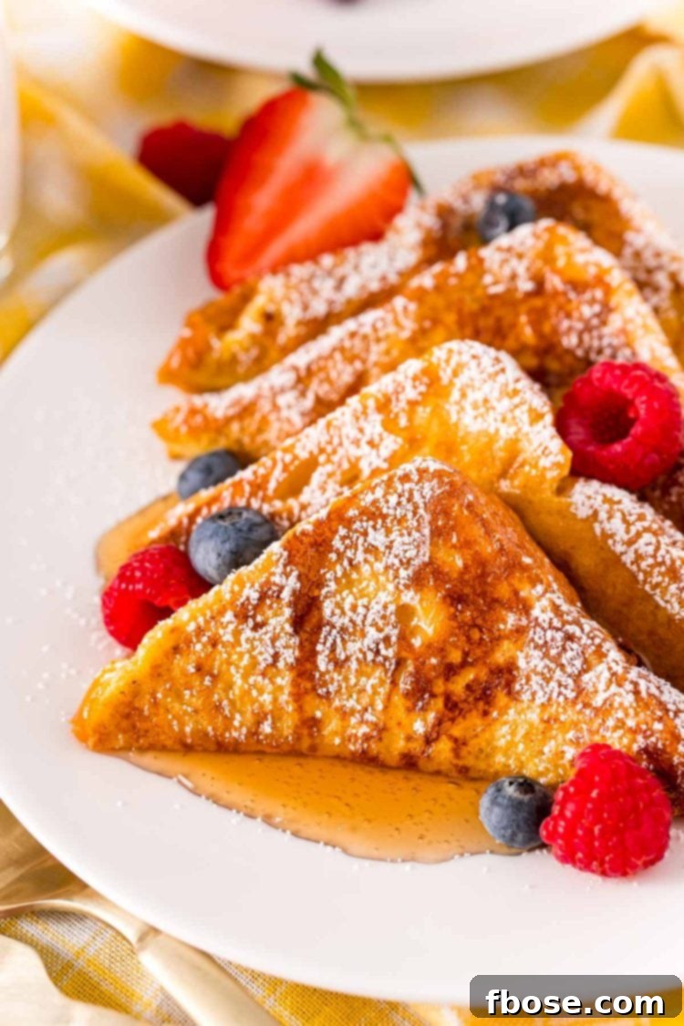 Close up photo of golden-brown French toast on a white plate with a side of fresh berries and a drizzle of maple syrup.