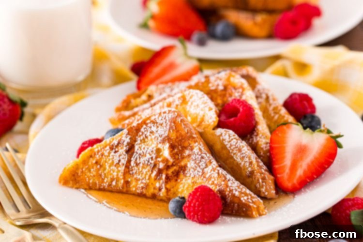 Close up photo of a single slice of brioche French toast on a white plate with fresh berries, showcasing its golden color and fluffy texture.
