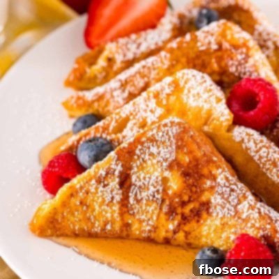 Close up photo of French toast on a white plate with berries and syrup.