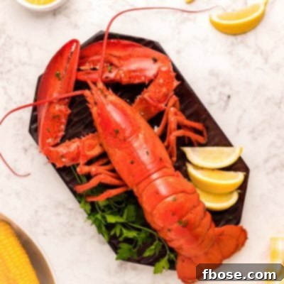 Overhead photo of a cooked lobster on a cutting board with lemon wedges and butter around it.