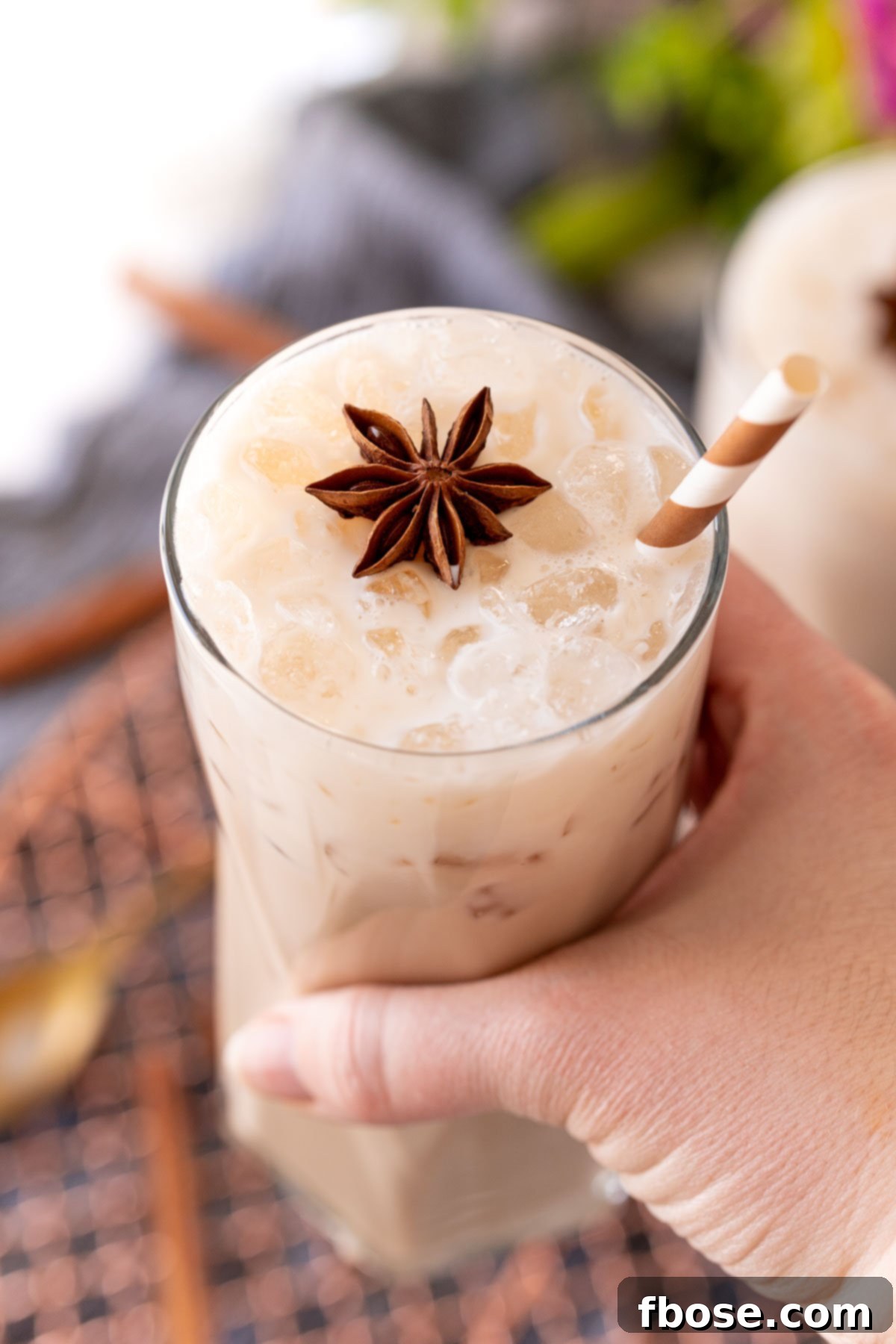A woman's hand holding a glass with an iced chai latte to the camera.