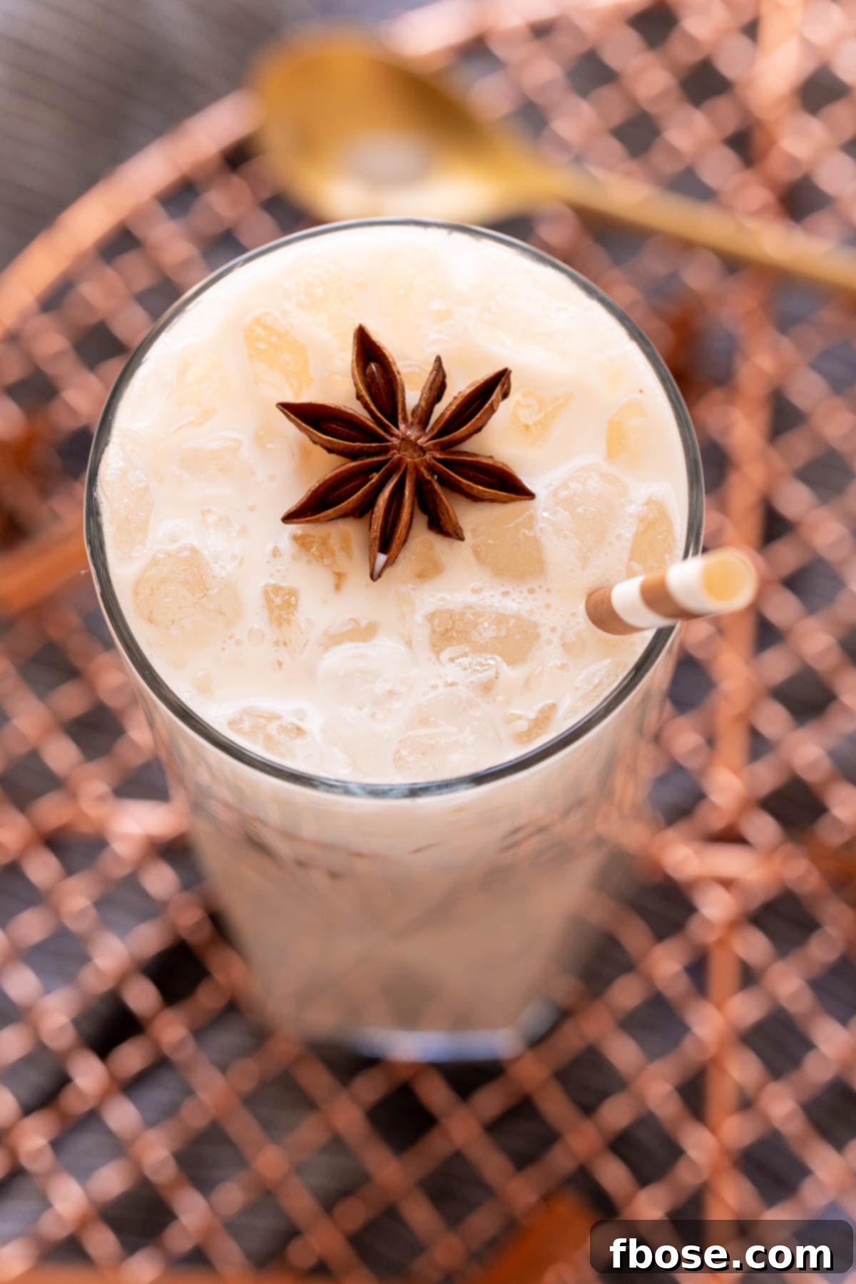 Close up photo of an iced chai tea latte on a copper wire rack garnished with star anise and a straw.