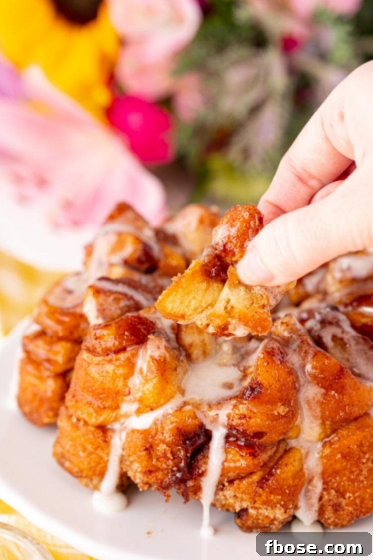 Close up photo of a woman's hand gently pulling a delicious, gooey piece of monkey bread from the main loaf.