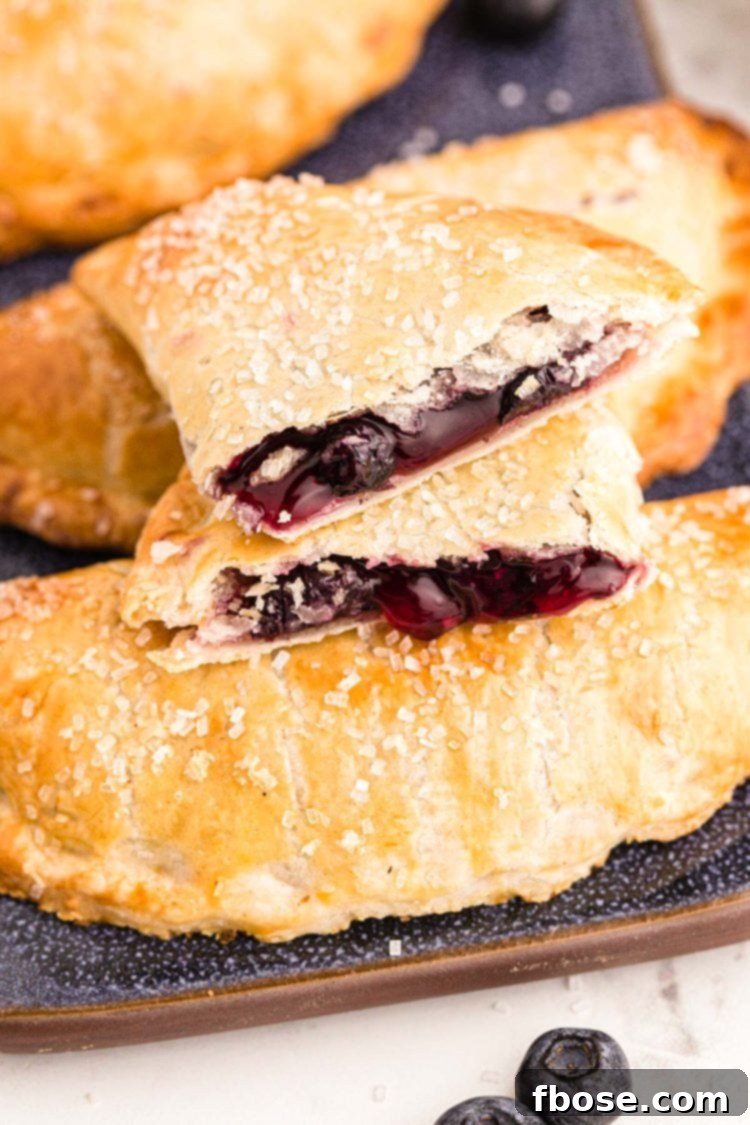 Close up photo of blueberry hand pies on a blue platter with one pie on top broken in half.