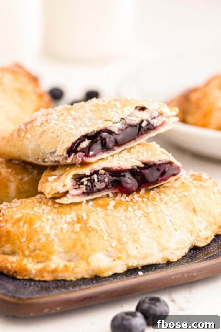 Photo of blueberry hand pies on a tray with a pie on top that's been split in half.