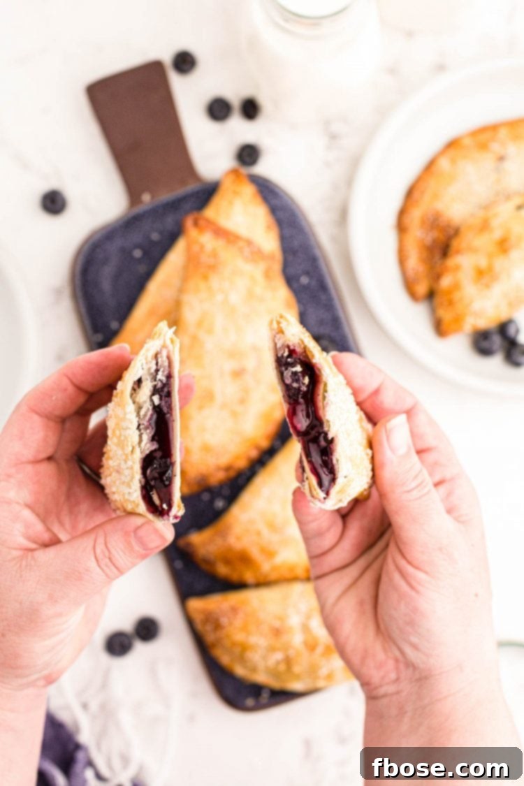 A woman's hands holding a blueberry hand pie that's been split in half.