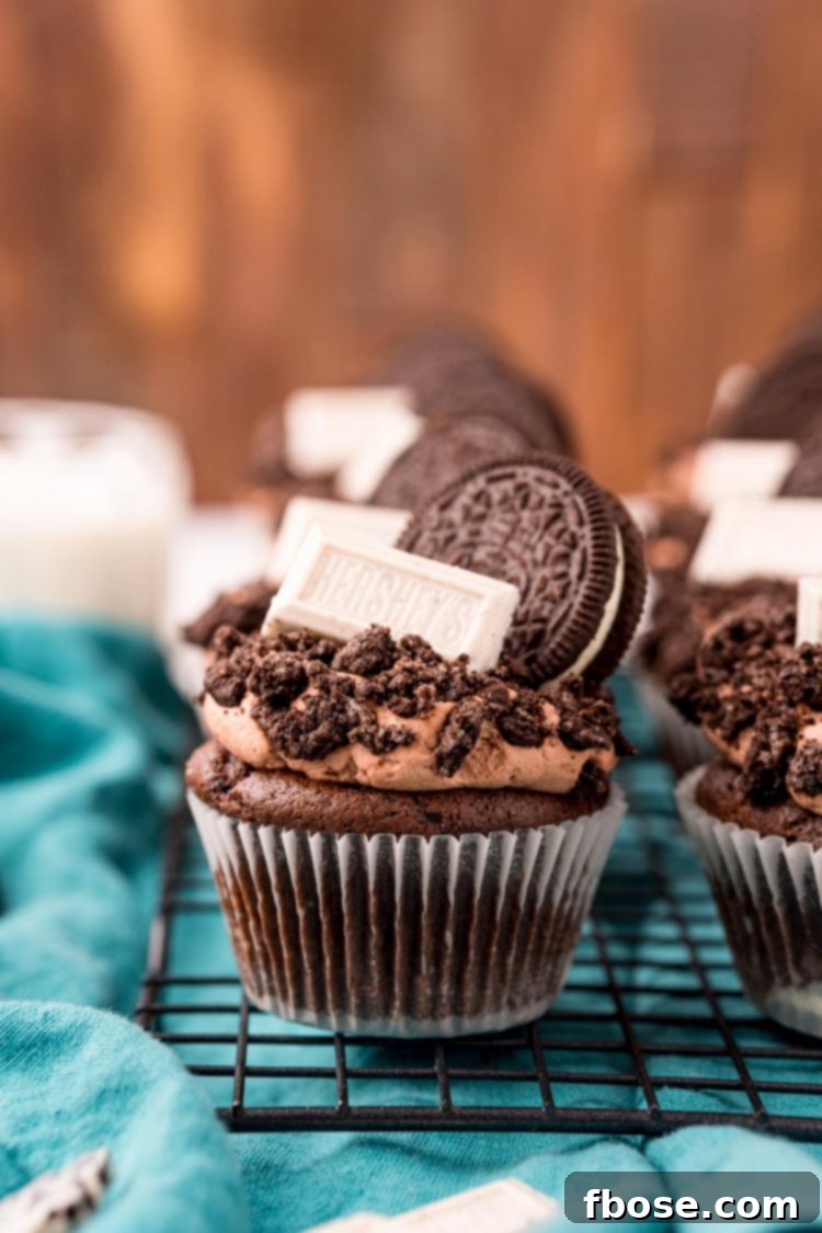 Close up of two Oreo Cupcakes on a wire rack on a blue napkin, highlighting the various Oreo elements.