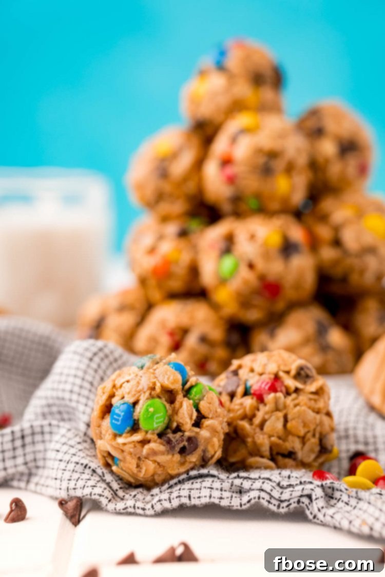 Close up photo of monster cookie energy balls on a table with a plate of them in the background with a glass of milk, highlighting their delicious appearance.