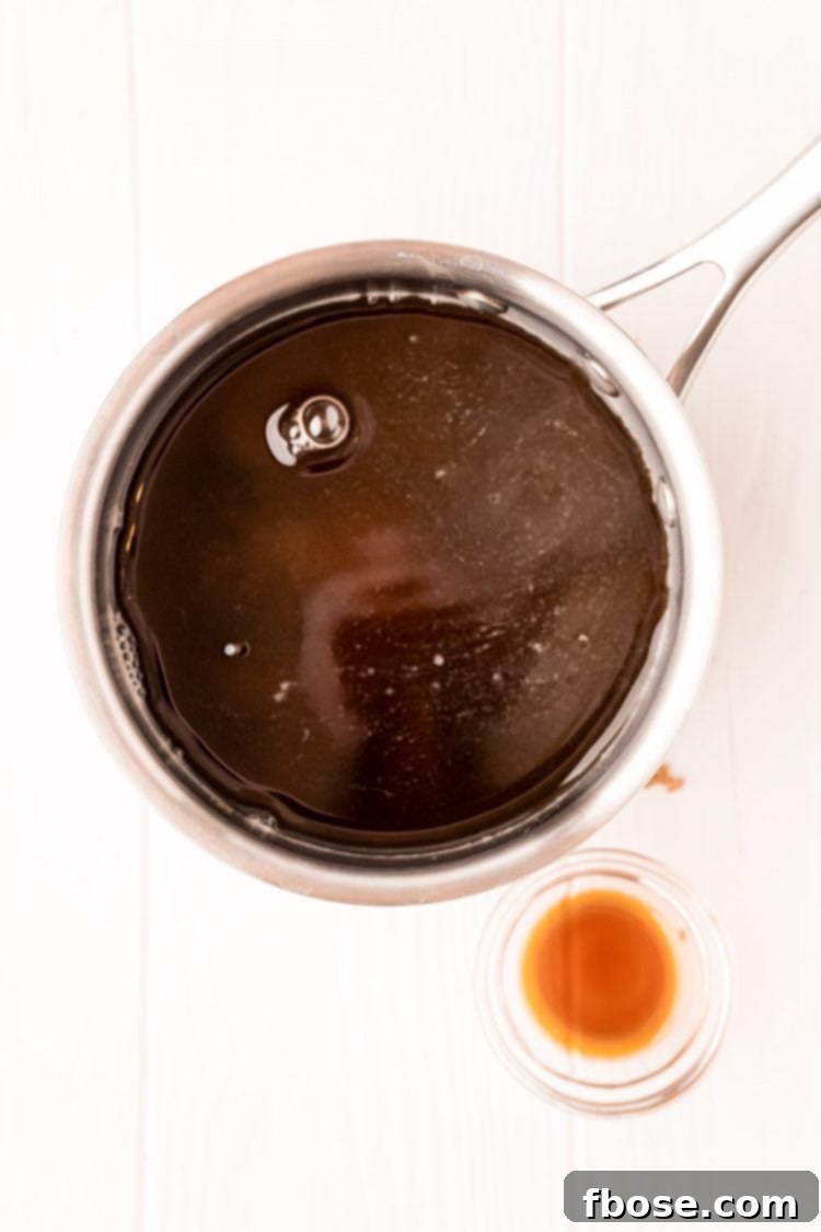 An overhead shot of a saucepan containing brown sugar simple syrup, with a small bowl of vanilla extract nearby.
