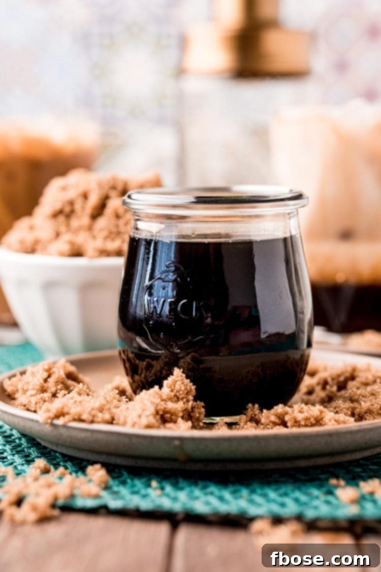 A beautifully composed close-up of a jar of brown sugar simple syrup, surrounded by loose brown sugar on a rustic brown plate.