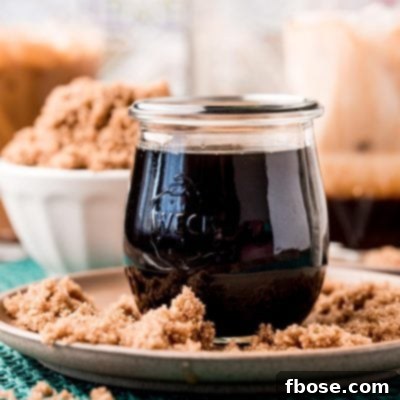 A close-up of a jar of brown sugar simple syrup on a brown plate with brown sugar all around it.