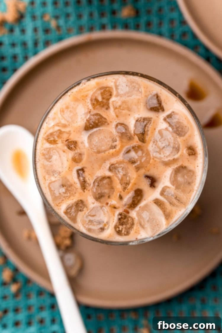 Close up photo of a brown sugar oatmilk shaken espresso on a brown plate with cinnamon sticks and brown sugar. The drink is in a tall glass, garnished with cinnamon, with a straw.