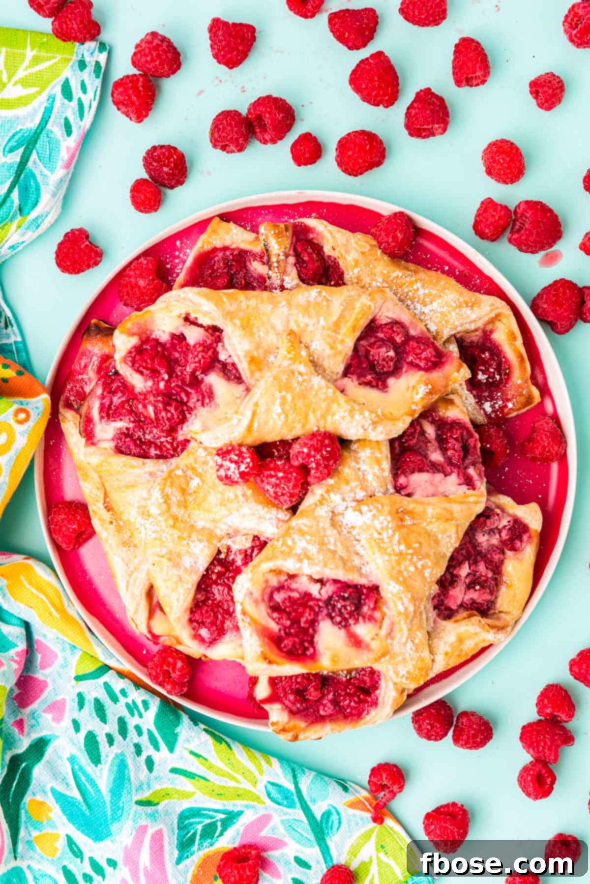 Overhead photo of raspberry danishes on a plate on a blue surface.