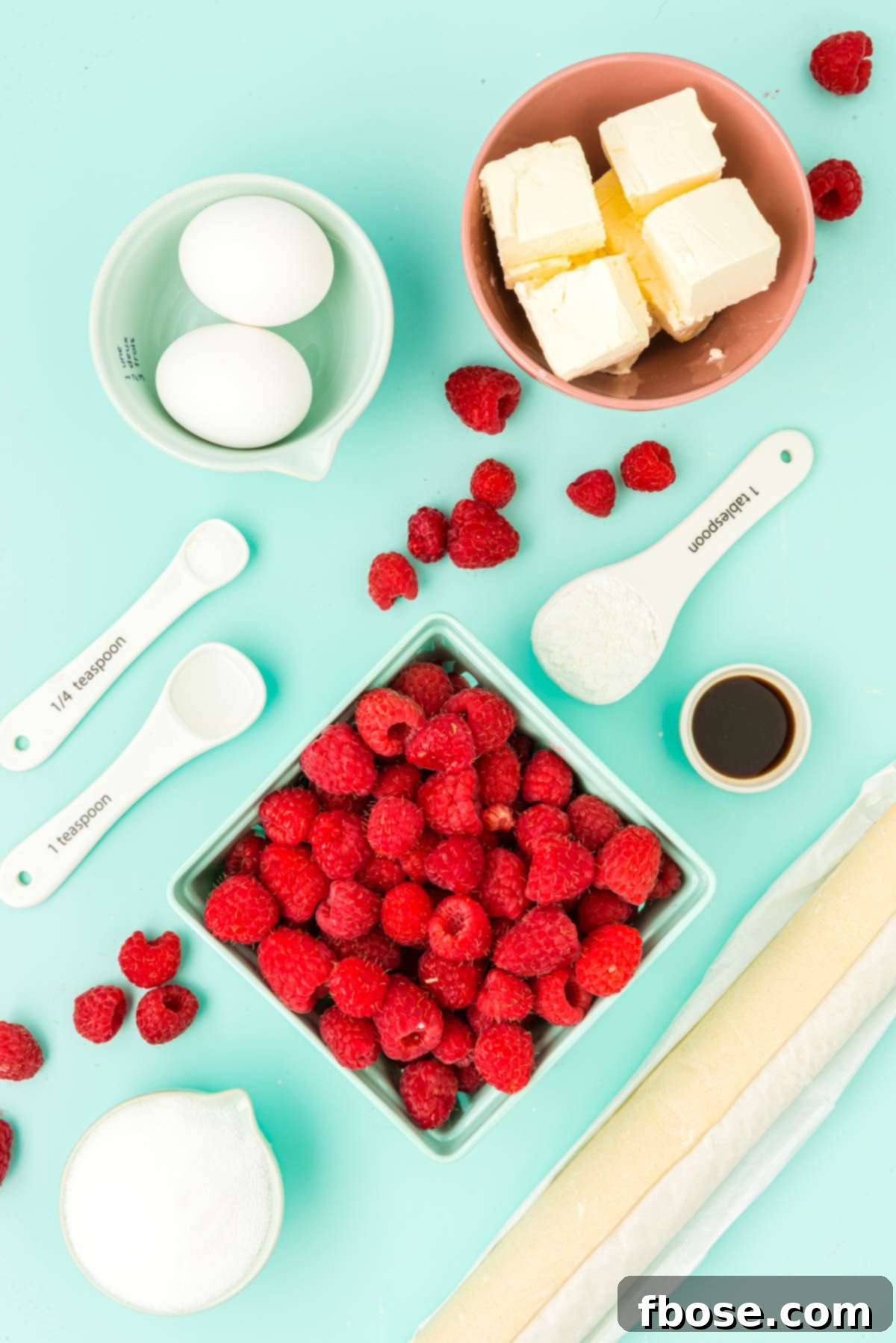Ingredients to make raspberry danishes prepared on a blue surface.