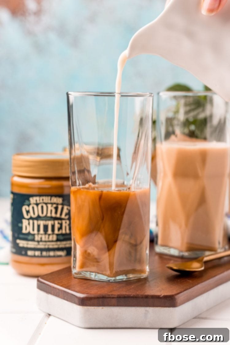The Viral TikTok Starbucks Secret Cookie Butter Latte 5 Oat milk being poured into a tall glass to make a cookie butter latte.