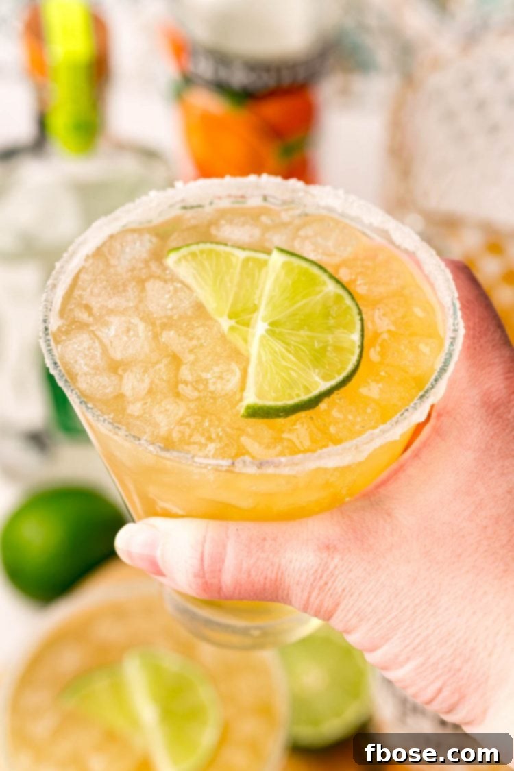 A woman's hand gracefully holding a chilled Beer Margarita glass, garnished with a lime, inviting a refreshing sip.