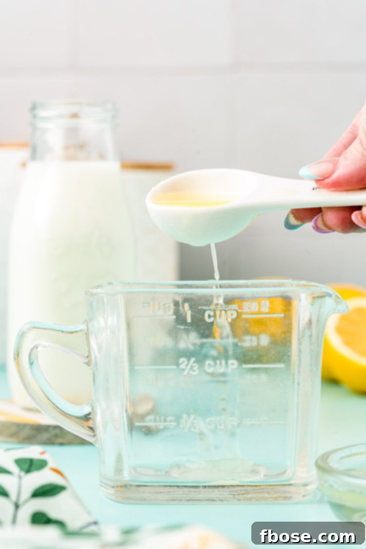 Lemon juice being added to a glass measuring cup with a measuring spoon.