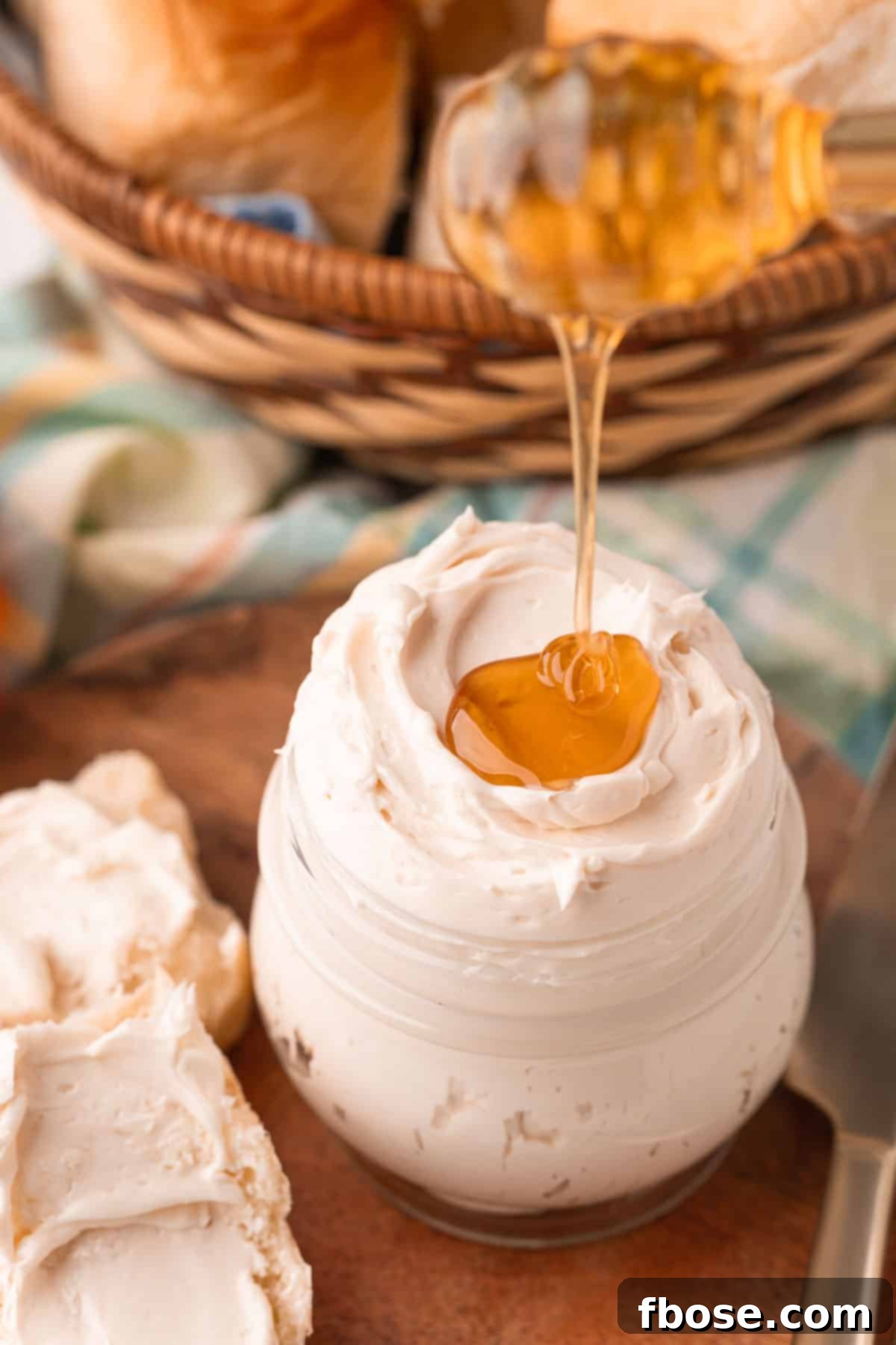 Honey being drizzled on top of a jar of whipped honey butter, highlighting its rich texture.