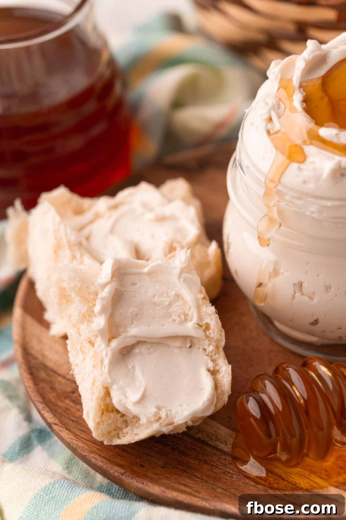 Dinner roll halves slathered with whipped honey butter next to a jar of it on a wooden plate, emphasizing its spreadable texture.